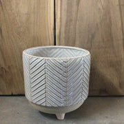 White and beige pot with lines leading together, bottom is round sandy with 3 small legs