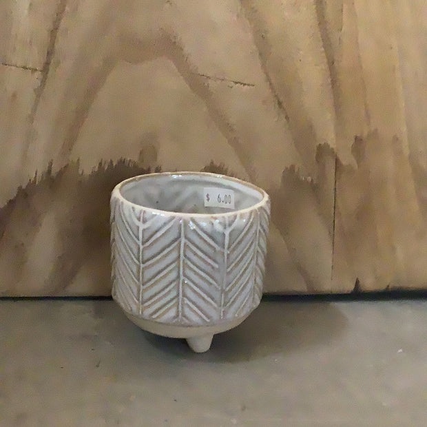 White and beige pot with lines leading together, bottom is round sandy with 3 small legs